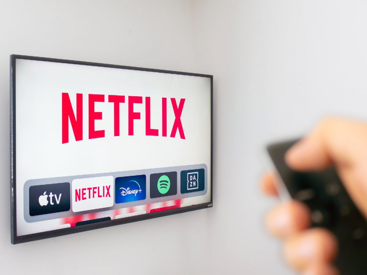 Una mano sostiene un control remoto apuntando a TV con Netflix en la pantalla