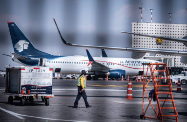 Avión de Aeroméxico en la pista del aeropuerto y un trabajador caminando. 