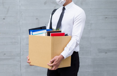Un hombre simula un despido de su trabajo al cargar una caja con sus pertenencias. 