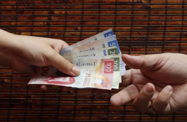Un par de manos intercambian billetes de pesos mexicanos.  