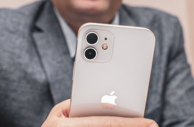 Una persona con saco color gris sostiene un iPhone 11 color blanco. 