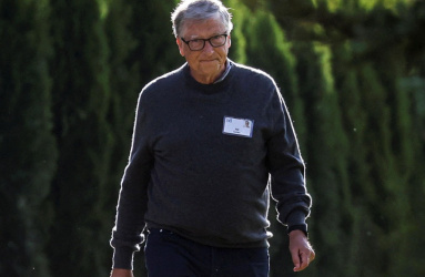 El empresario Bill Gates camina en un jardín al utilizar un suéter color gris y un pantalón azul. 