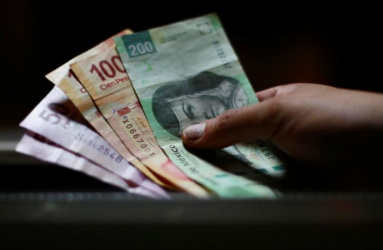 Una mano sostiene billetes de 200, 100 y 50 pesos mexicanos en un fondo oscuro. 
