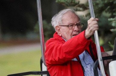 El multimillonario Warren Buffett sentado en un carrito de golf y viste una chamarra color rojo. 