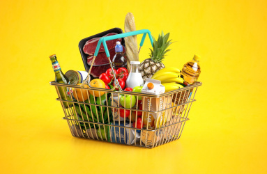 Una canasta de supermercado con distintos productos alimenticios, detrás hay un fondo color amarillo.  