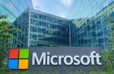 Letrero de la empresa Microsoft colocado sobre un jardín, detrás hay un edificio de cristales. 