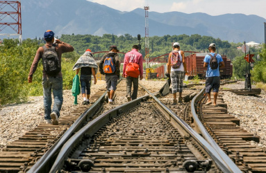frontera de Estados Unidos/México con personas migrantes caminando sobre vías de tren