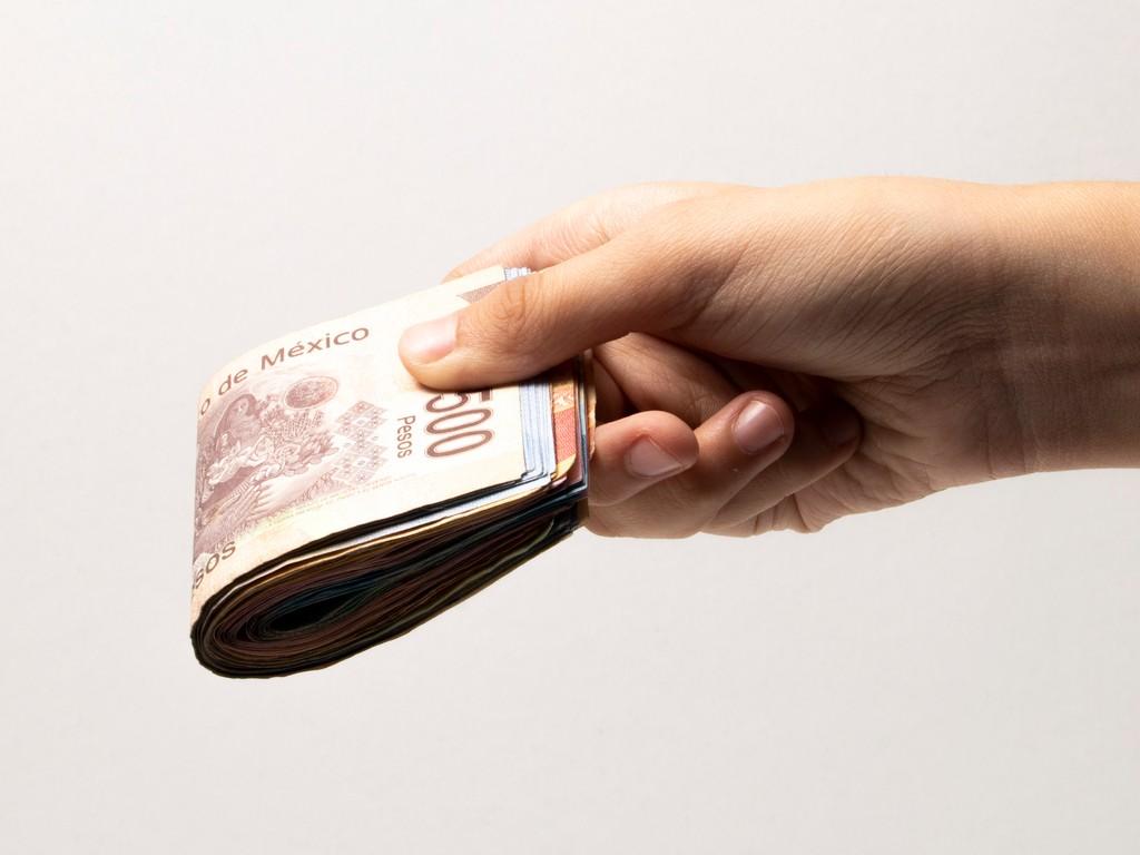 Una mano sostiene un fajo de billetes mexicanos. 