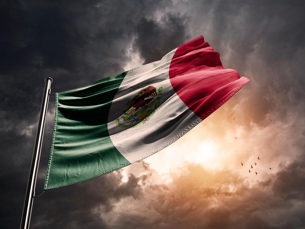 Una bandera de México en el hasta con un cielo muy nublado simulando una tormenta. 