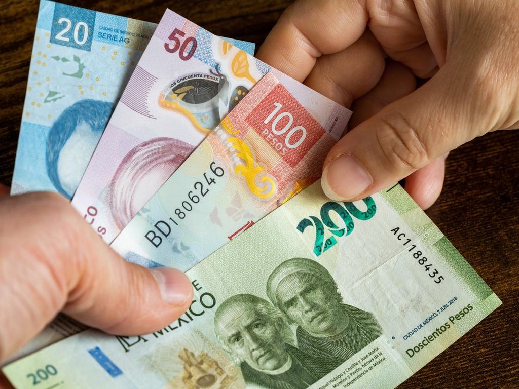 Dos manos intercambian billetes de 200, 100, 50 y 20 pesos mexicanos. 