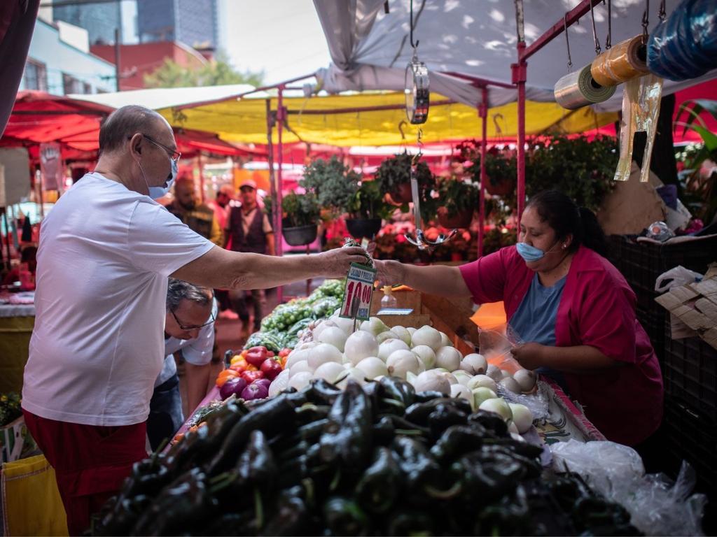 Un hombre compra verduras en un puesto de mercado popular y una señora lo atiende. 