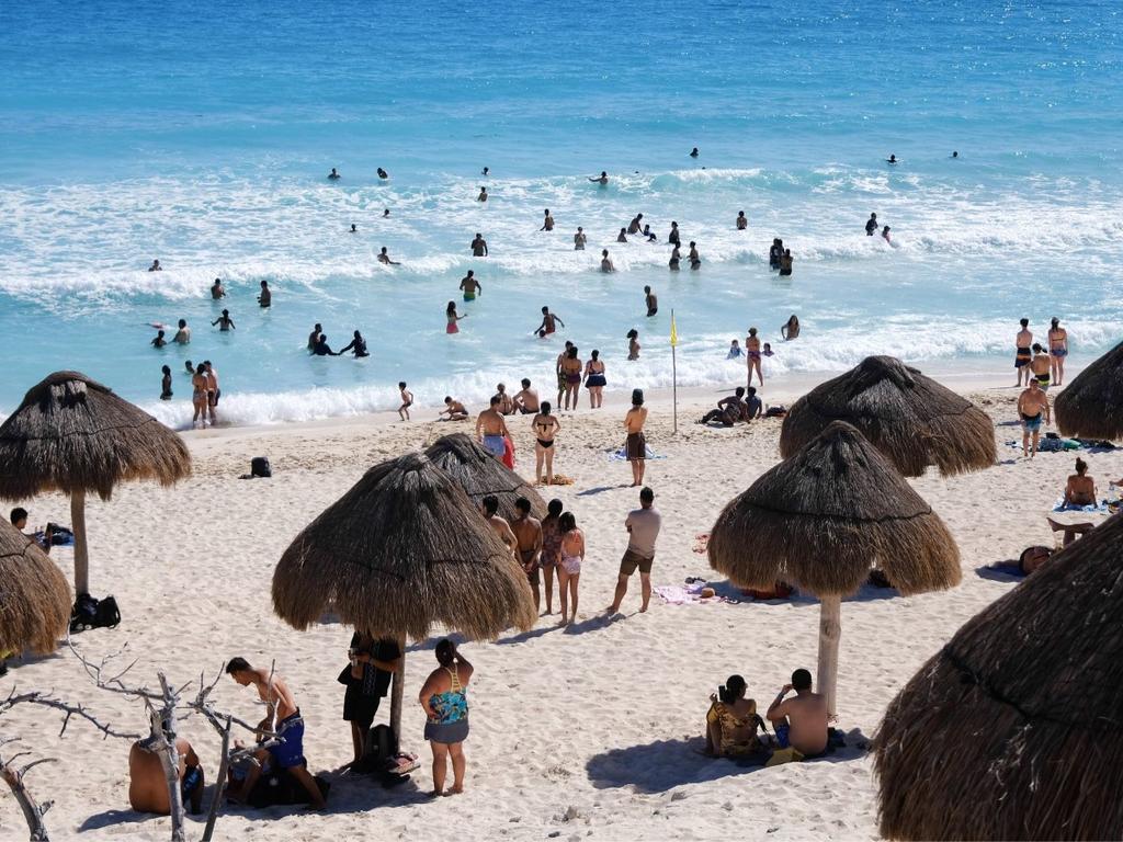 Orilla de una playa en Cancún con turistas y sombrillas. 