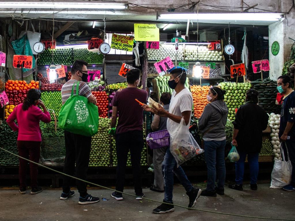 Varias personas comprando verduras en un puesto de mercado popular mexicano. 
