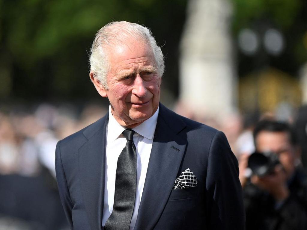 Rey Carlos III de pie con traje color oscuro, camisa blanca y corbata negra. 