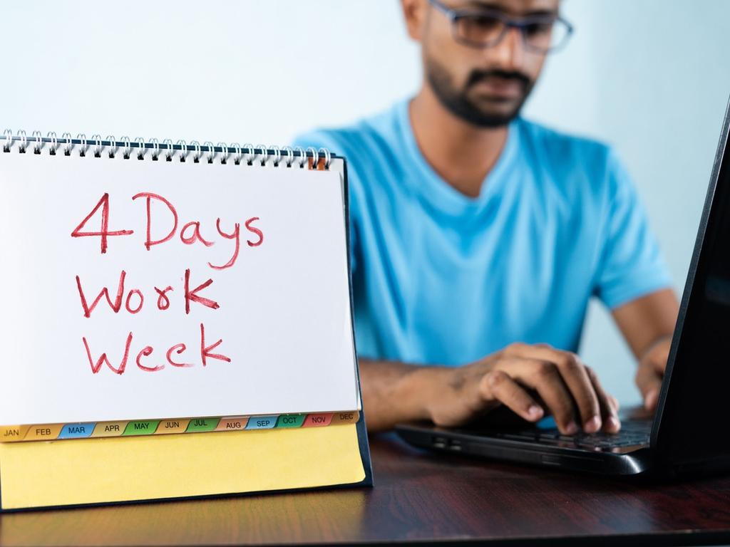 Un hombre de lentes y barba utiliza una laptop sobre un escritorio, a un lado hay un tipo calendario con la leyenda de 4 días laborales a la semana. 