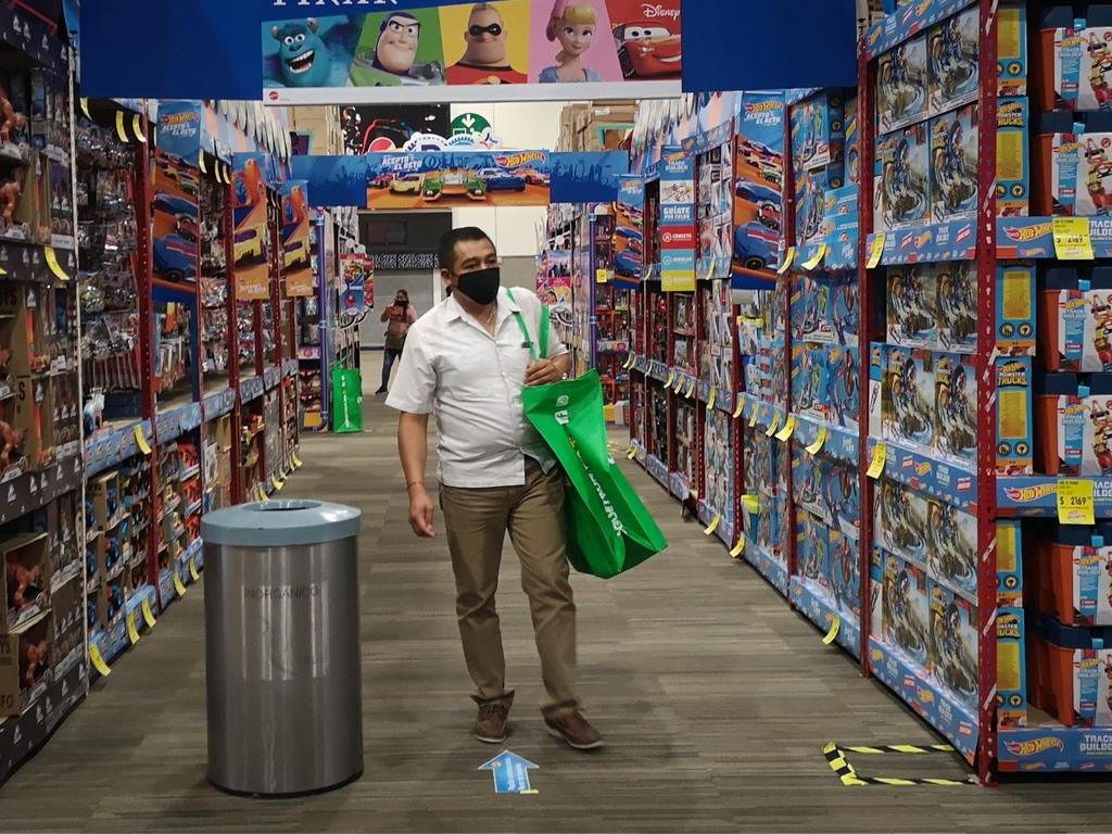 Un hombre parado en una tienda de juguetes y sostiene una bolsa color verde. 