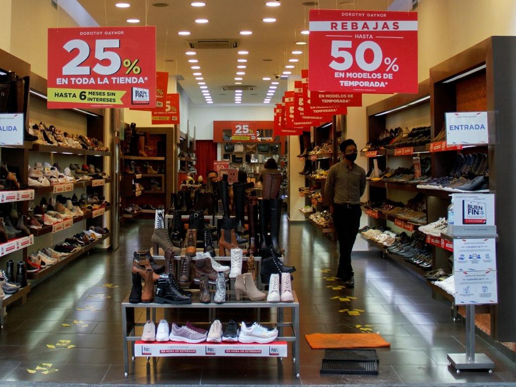 Un tienda de zapatos con una persona caminando y letreros rojos de descuentos. 