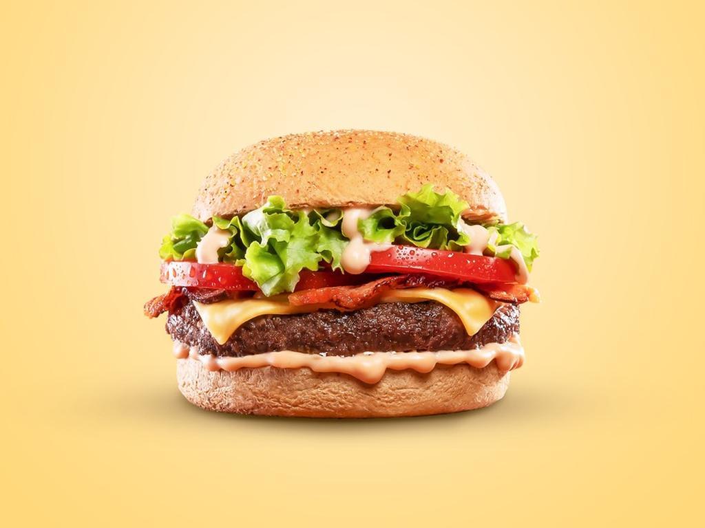 Una hamburguesa con lechuga, jitomate, tocino, carne y queso, colocada sobre un fondo color amarillo. 