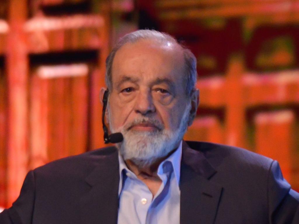 El empresario Carlos Slim sonríe al estar sentado en un escenario y utiliza un micrófono de diadema. 