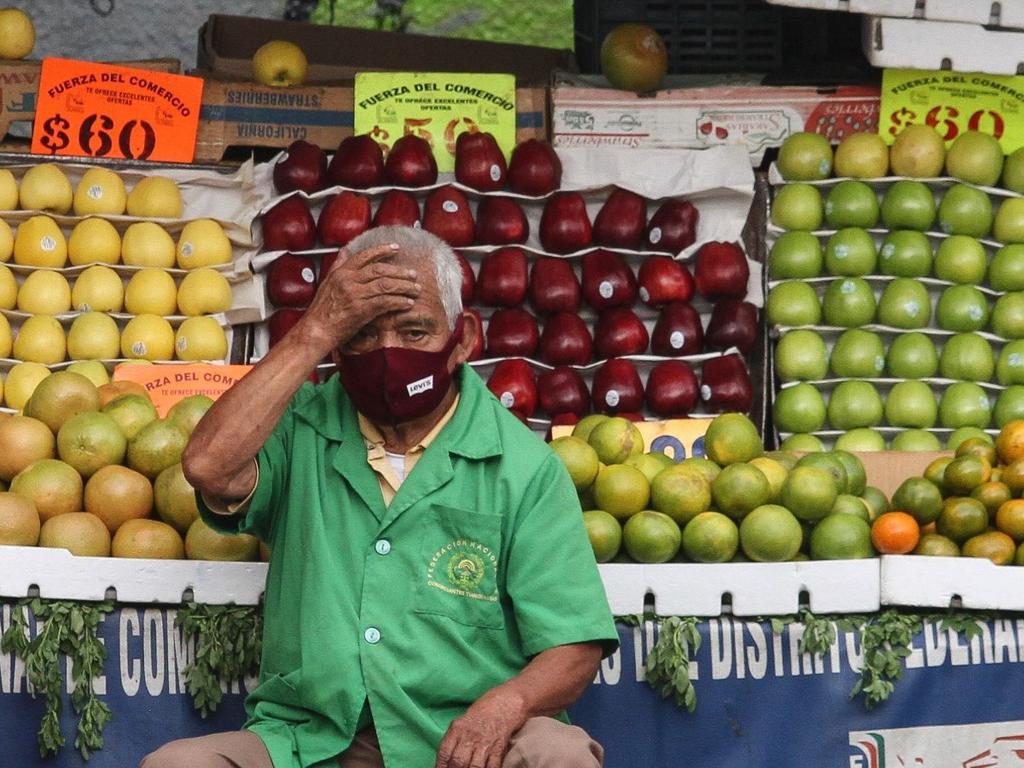 Un hombre adulto mayor expresa preocupación al estar sentado frente a un puesto de fruta.  