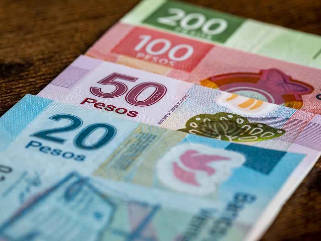 Billetes de 200, 100, 50 y 20 pesos mexicanos, colocados uno encima de otro sobre una superficie color café. 