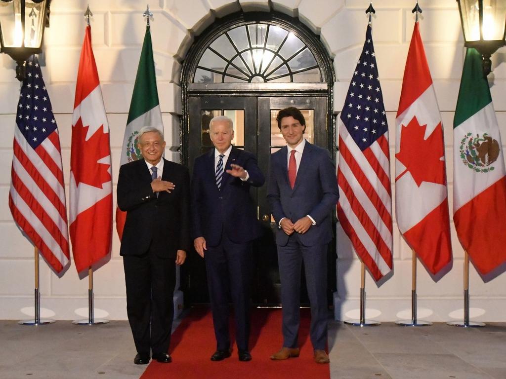 López Obrador, Joe Biden y Justin Trudeau posan frente a una puerta color negro, detrás están las banderas de México, Estados Unidos y Canadá. 