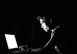 Hombre sentado en la oscuridad con computadora encendida