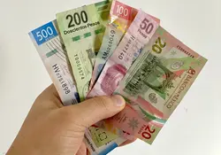 Una mano sostiene 5 billetes de pesos mexicanos (uno de 500, uno de 200, uno de 100, uno de 50 y uno de 20 pesos). 