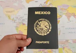 Mano sosteniendo pasaporte mexicano sobre mapa. 