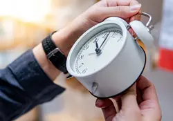 Las manos de una persona sostienen un reloj blanco y cambian la hora. 
