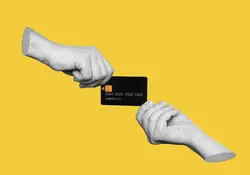 Un par de manos sostienen una tarjeta de crédito color negro y fondo amarillo. 