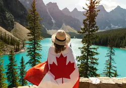 mujer de espaldas envuelta en la bandera de canda con paisaje de bosque, montañas y rio de fondo