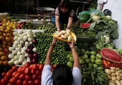 Dos señoras en un mercado intercambiando verduras sobre puesto de verduras