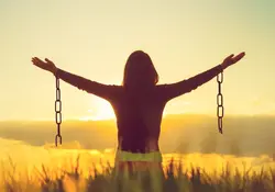 Mujer con brazos extendidos en señal de libertad con cadenas rotas colgando en entorno natural