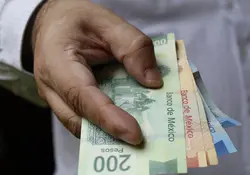 Una mano sostiene billetes de 200, 100 y 20 pesos mexicanos. 