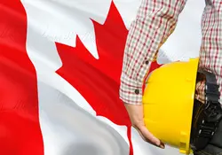 Hombre sosteniendo casco de seguridad amarillo con el fondo de la bandera de Canadá