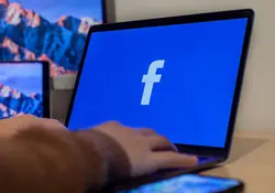 computadora sobre escritorio con fondo de pantalla azul y logo de facebook 