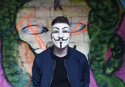 Persona parada frente a muro con mascara de anonymous