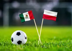 Pequeñas banderas de México y Polonia en una cancha de césped y un mini balón de fútbol al costado. 