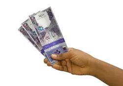 Una mano sostiene billetes de la moneda rial de Catar en color morado. 