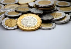 Monedas de pesos mexicanos en color plateado y dorado amontonadas sobre un fondo blanco. 