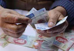 Dos manos sostienen billetes de 500 pesos color azul y en la parte de abajo hay más billetes de 100 y 20 pesos. 
