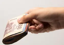 Una mano sostiene un fajo de billetes de pesos mexicanos. 