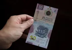 Una mano sostiene un billete de 50 pesos mexicanos con un fondo color negro. 