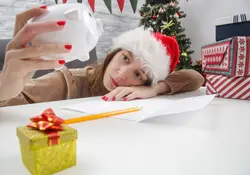 Una mujer triste sostiene una alcancía de cerdito al estar recargada sobre una mesa y con adornos de navidad alrededor. 