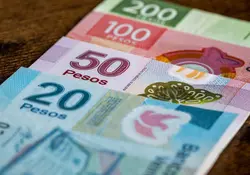 Billetes de 200, 100, 50 y 20 pesos mexicanos, colocados uno encima de otro sobre una superficie color café. 