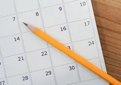 calendario de papel blanco con lápiz amarillo encima, sobre mesa de madera