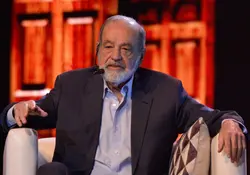 El empresario Carlos Slim hablando con un micrófono de diadema y sentado en un sillón. 