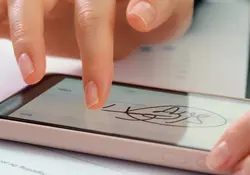 Una mano escribe su firma sobre la pantalla de un dispositivo móvil. 