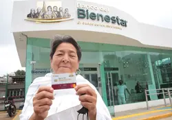 Mujer fuera del banco del bienestar con una tarjeta del banco en las manos